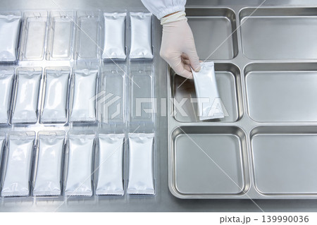 Gloved hand places sealed sachet into sterile compartmentalized tray for packaging 139990036