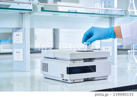 Scientist in blue gloves places sample vial into laboratory analysis equipment Scientist in blue gloves places sample vial into laboratory analysis equipment 139990135