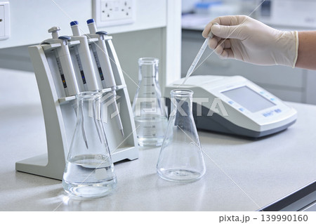 Scientist performing liquid handling with pipettes and flasks in a laboratory setting Scientist performing liquid handling with pipettes and flasks in a laboratory setting 139990160