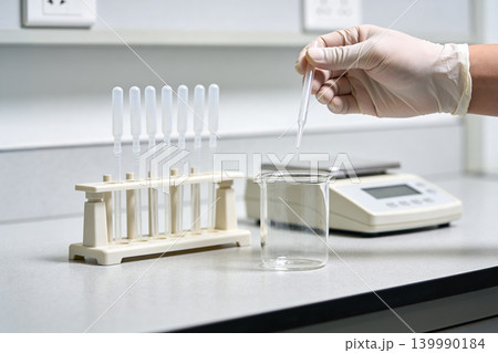 Scientist performing liquid transfer with a dropper into a beaker in a laboratory setting Scientist performing liquid transfer with a dropper into a beaker in a laboratory setting 139990184