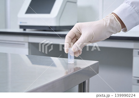 Scientist in sterile gloves places a small vial on a stainless steel laboratory bench Scientist in sterile gloves places a small vial on a stainless steel laboratory bench 139990224