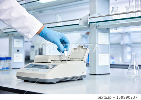 Scientist in blue gloves places sample tube into laboratory heating device 139990237