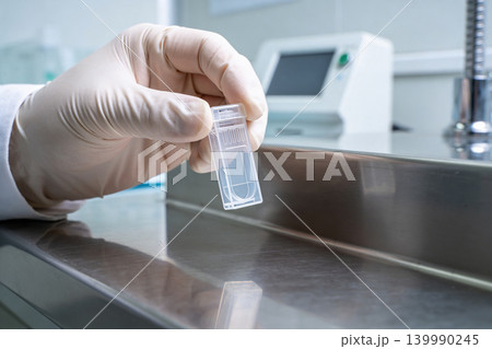 Scientist in sterile gloves holds a small transparent sample container in a laboratory setting 139990245