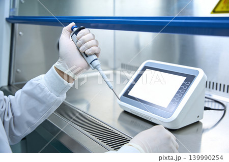 Scientist in sterile lab coat and gloves uses pipette with digital device Scientist in sterile lab coat and gloves uses pipette with digital device 139990254
