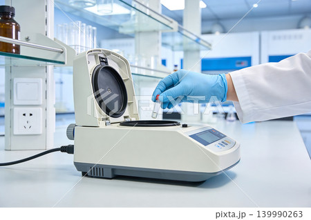 Scientist in blue gloves places vial into laboratory centrifuge for analysis 139990263