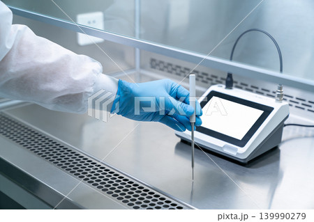Scientist in sterile lab coat and gloves uses probe with digital device Scientist in sterile lab coat and gloves uses probe with digital device 139990279