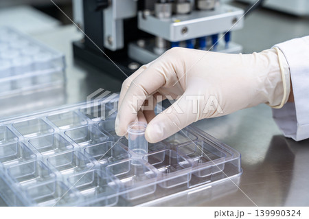 Scientist in lab coat and gloves carefully places small vial into multi-well plate Scientist in lab coat and gloves carefully places small vial into multi-well plate 139990324