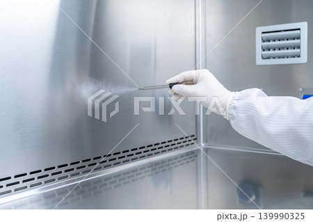 Scientist in sterile lab coat and gloves sprays mist from a device in a cleanroom 139990325