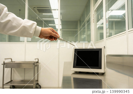 Scientist in lab coat uses thermometer probe near digital display in cleanroom Scientist in lab coat uses thermometer probe near digital display in cleanroom 139990345