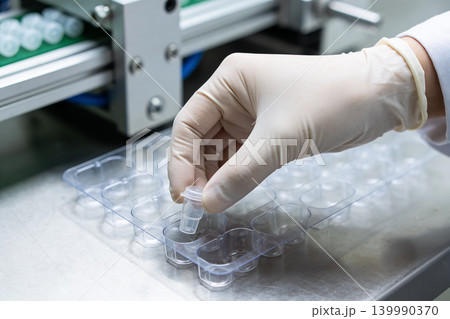 Scientist in sterile gloves places small vial into a laboratory tray for testing Scientist in sterile gloves places small vial into a laboratory tray for testing 139990370
