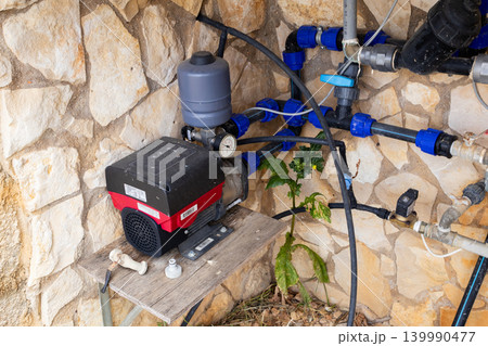 Water pump system with pressure tank and plumbing on a stone wall background Water pump system with pressure tank and plumbing on a stone wall background 139990477