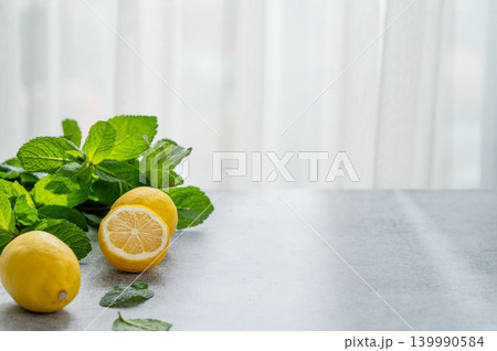 Fresh lemons with mint leaves on light table in bright natural setting. Fresh lemons with mint leaves on light table in bright natural setting. 139990584