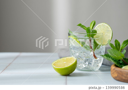 A fresh mojito with lime, mint and ice in glass. Citrus lemonade or cocktail on a table A fresh mojito with lime, mint and ice in glass. Citrus lemonade or cocktail on a table 139990586