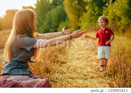 Young mother stretches out her hands to her two-year-old son in the field 139991923