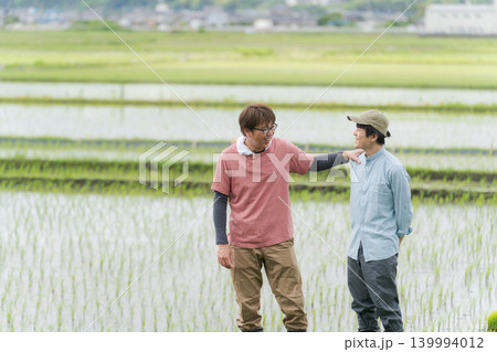 田んぼの畦道に立つ2人の農家 139994012