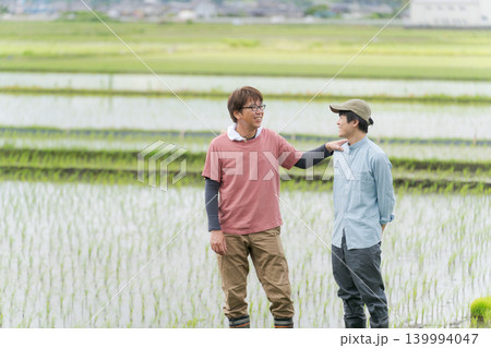 田んぼの畦道に立つ2人の農家 139994047