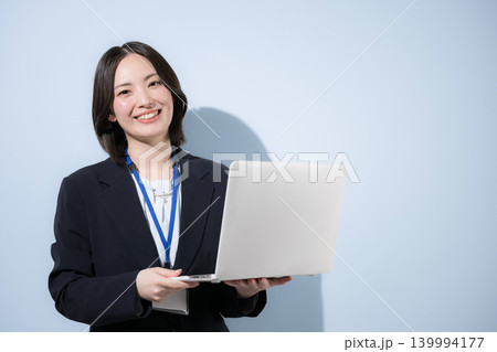 水色背景で名札をつけたノートパソコンを持つ働く女性社員のビジネスとITなどのイメージ カメラ目線笑顔 水色背景で名札をつけたノートパソコンを持つ働く女性社員のビジネスとITなどのイメージ カメラ目線笑顔 139994177