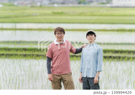 田んぼの畦道に立つ20代と50代の農家 田んぼの畦道に立つ20代と50代の農家 139994420
