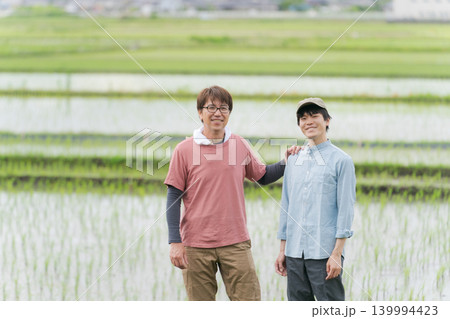 田んぼの畦道に立つ20代と50代の農家 田んぼの畦道に立つ20代と50代の農家 139994423