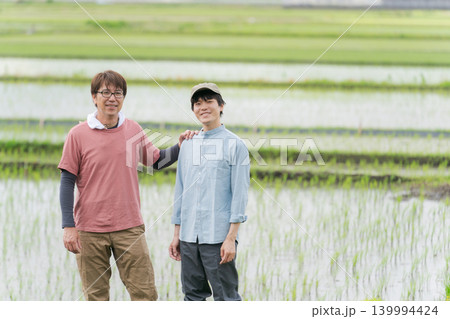 田んぼの畦道に立つ20代と50代の農家 田んぼの畦道に立つ20代と50代の農家 139994424