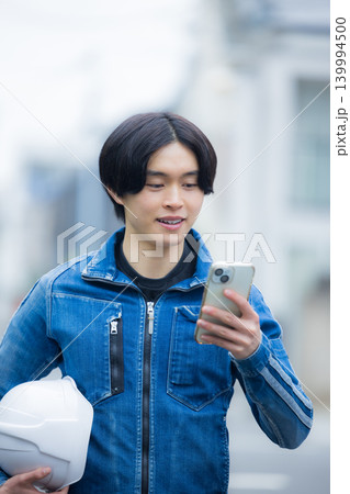 スマホを操作する若い作業員　 139994500