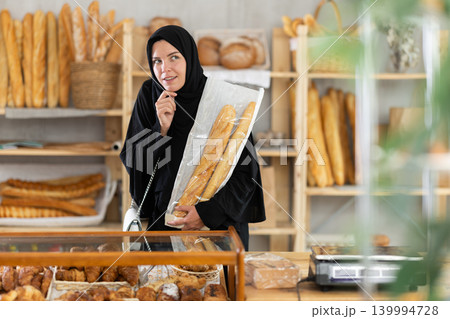 Young woman in Muslim clothing choosing pastries in bakery Young woman in Muslim clothing choosing pastries in bakery 139994728