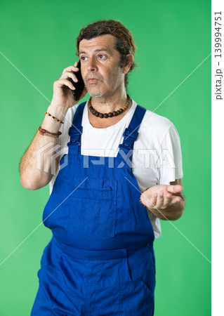 Male person wearing in blue overall is talking on phone 139994751