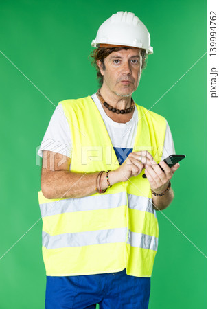Man wearing in reflective vest and hard hat scrolls phone screen Man wearing in reflective vest and hard hat scrolls phone screen 139994762