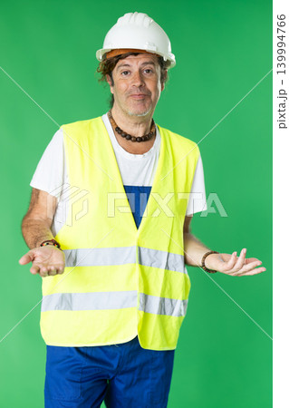 Man in reflective vest and hard hat on green background speaks imaginary partner. Man in reflective vest and hard hat on green background speaks imaginary partner. 139994766