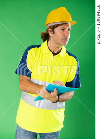 Adult man in reflective polo shirt and hard hat holding inventory documents on green screen 139994816