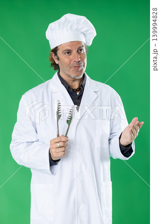 Adult male cook holding pastry tongs and explaining baking technique on green screen 139994828