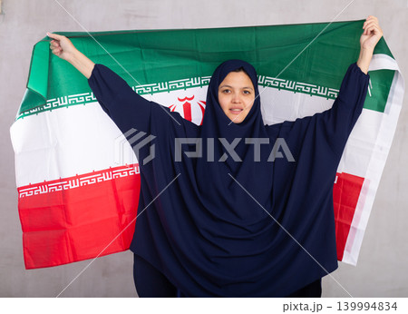 Young Muslim woman in blue hijab holds unfurled flag of Iran. 139994834