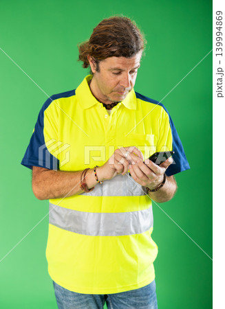 Adult man in reflective polo shirt using smartphone for inventory on green screen 139994869