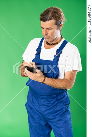 Handyman in overalls responds to customer messages on green background Handyman in overalls responds to customer messages on green background 139994877