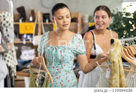 Near rack, female friends buy summer clothes, choose some items Near rack, female friends buy summer clothes, choose some items 139994886