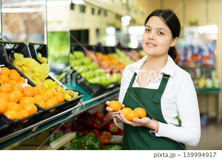 Young woman in uniform sells tangerines in grocery store Young woman in uniform sells tangerines in grocery store 139994917