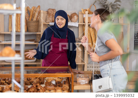 Smiling Arab saleswoman talking to female customer in bakery Smiling Arab saleswoman talking to female customer in bakery 139995032