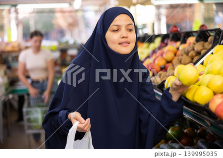 Woman in paranja shopping and choosing local juicy apples in hypermarket Woman in paranja shopping and choosing local juicy apples in hypermarket 139995035