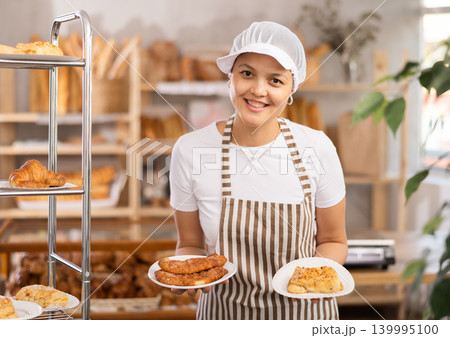 Middle-aged saleswoman displays pastry in plates Middle-aged saleswoman displays pastry in plates 139995100