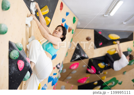 Sporty woman climbing on bouldering wall demonstrating physical strength, technical skill, and determination Sporty woman climbing on bouldering wall demonstrating physical strength, technical skill, and determination 139995111