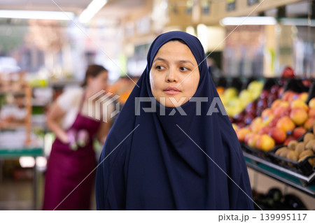Portrait of young woman in veil, walking with a shopper cart, making necessary purchases 139995117