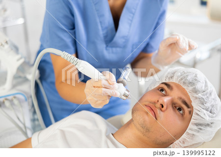 Young woman cosmetologist doing moisturizing procedure to young man Young woman cosmetologist doing moisturizing procedure to young man 139995122
