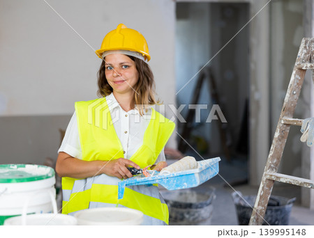 Portrait of woman painter in a protective helmet and vest with paint roller Portrait of woman painter in a protective helmet and vest with paint roller 139995148