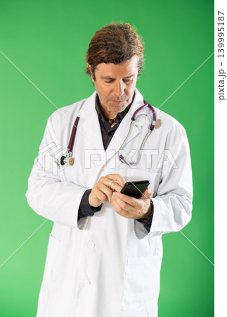 Adult male medic in white coat scrolling smartphone on green screen 139995187