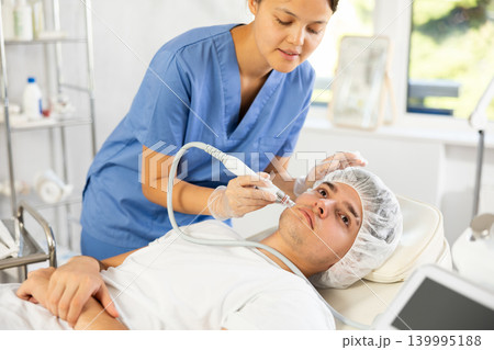 Young woman cosmetologist doing cleansing procedure to young man 139995188
