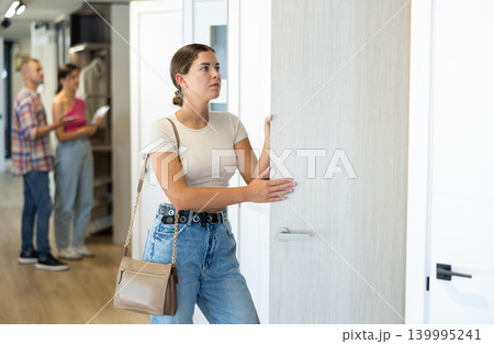 Young female buyer carefully selects an interior door in hardware store Young female buyer carefully selects an interior door in hardware store 139995241