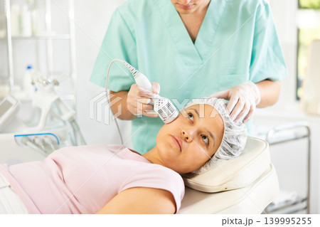 Young male cosmetologist doing whitening procedure to young woman 139995255