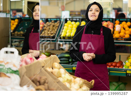 Portrait of friendly female salesperson in hijab and apron in grocery section of supermarket Portrait of friendly female salesperson in hijab and apron in grocery section of supermarket 139995287
