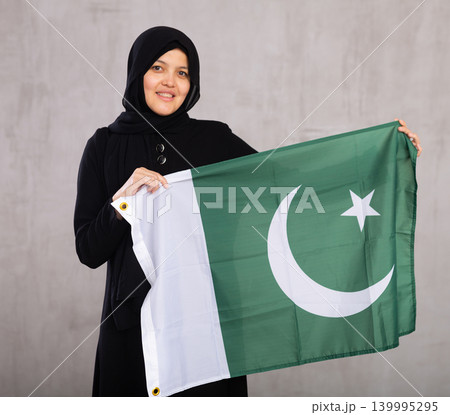 Young Muslim woman in black hijab holds unfurled flag of Pakistan. 139995295