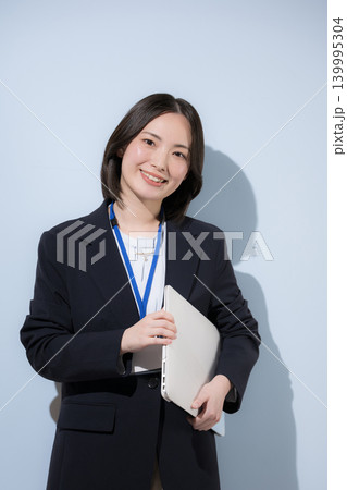 水色背景で名札をつけたノートパソコンを持つ働くかわいい女性社員のビジネスとITイメージ　カメラ目線 139995304